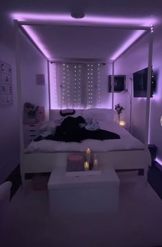 a white bed sitting under a purple light next to a table with candles on it