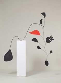 a white vase with black and red flowers in it next to a tall white box