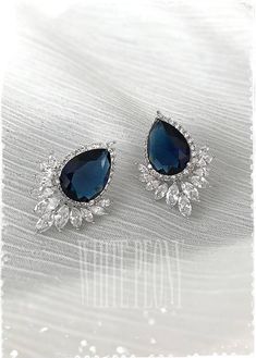 two pairs of blue and white diamond earrings on top of a white cloth with the words,