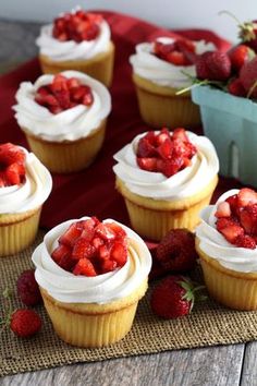 several cupcakes with white frosting and strawberries on the top are sitting on a mat