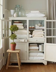 a white cabinet filled with lots of folded towels and other items next to a window