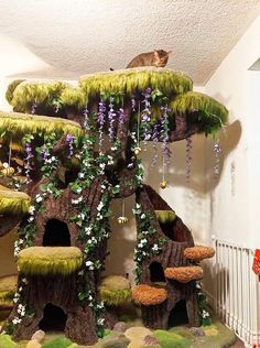 a cat sitting on top of a tree house made out of fake grass and flowers