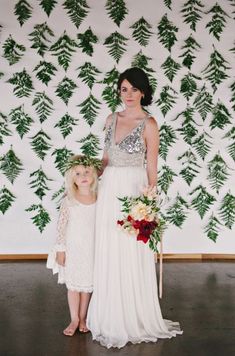 a mother and daughter standing in front of a wall with green leaves on it