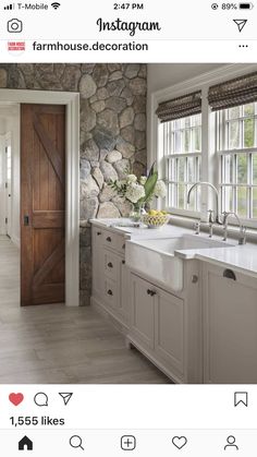 a kitchen with stone walls and white cabinets is pictured in this image, there are flowers on the window sill