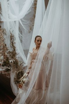 a woman standing in front of a white curtain with flowers on it and holding her hands out