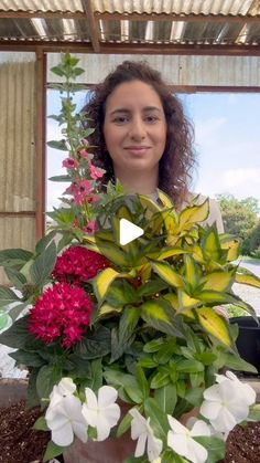 a woman standing in front of a potted plant with flowers on it and smiling at the camera