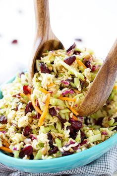 a blue bowl filled with rice salad and two wooden serving spoons in the bowl