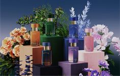 an assortment of perfume bottles sitting on top of blocks in front of flowers and greenery