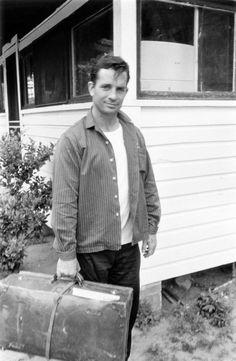 black and white photograph of a man holding a suit case in front of a house