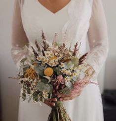 a woman holding a bouquet of flowers in her hands and wearing a white dress with sheer sleeves