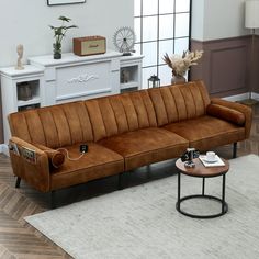 a brown leather couch sitting on top of a wooden floor next to a table and chair