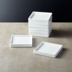 six white square plates stacked on top of each other in front of a black wall