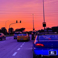 several cars are stopped at an intersection as the sun is setting in the sky behind them