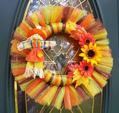 a colorful wreath with flowers and a scarecrow on the front door for halloween time