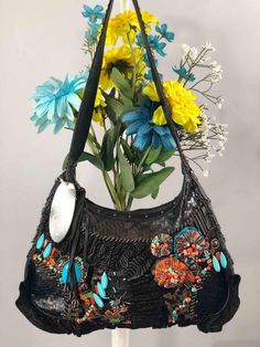 a black purse with blue and yellow flowers in it sitting on a white stand next to a gray wall