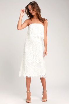 a woman is wearing a white dress with lace on the bottom and side, she has her hand in her hair