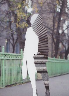 a man walking down the street in front of a spiral stair case with trees behind him