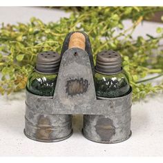 two metal containers with green liquid in them sitting on a table next to some plants