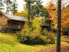 a cabin in the woods surrounded by trees and grass with fall foliage on the ground