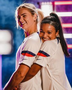 two female tennis players hugging each other in front of a blue and purple wall with lights behind them