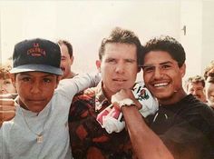 three young men posing for a photo with one holding a bottle and the other wearing a baseball cap