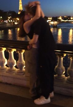 two people standing next to each other in front of the eiffel tower at night