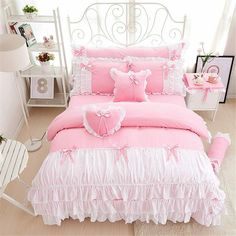 a bed with pink comforter and pillows in a white room next to a window