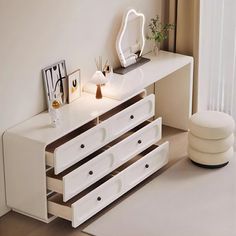 a white dresser with three drawers next to a mirror and vase on top of it