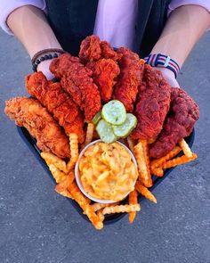 a person holding a plate with fried chicken and french fries