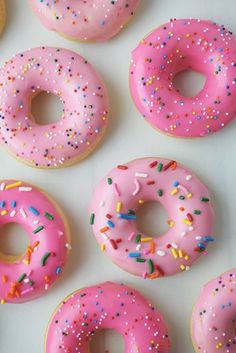 pink frosted donuts with sprinkles arranged on a white surface, top view