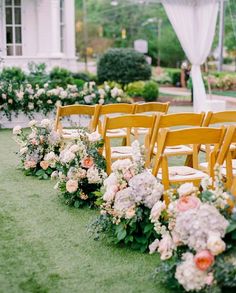 rows of wooden chairs lined up with flowers and greenery in front of a building