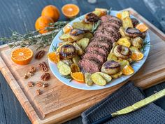 a white plate topped with meat and veggies next to sliced oranges on a cutting board