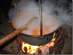 a large pot is cooking over an open fire with two wooden spoons sticking out of it