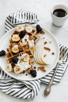 a white plate topped with waffles and fruit next to a cup of coffee