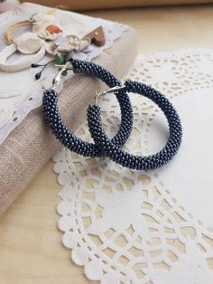 two pairs of beaded hoop earrings sitting on top of a doily next to a book