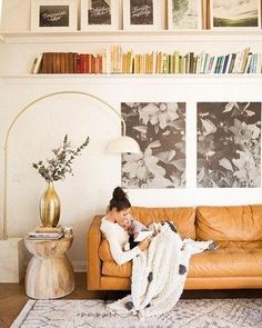 a woman laying on top of a couch in a living room next to a book shelf