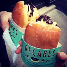 two people holding ice cream sandwiches with chocolate toppings in paper cups on the street