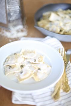 a white plate topped with ravioli on top of a wooden table next to silverware