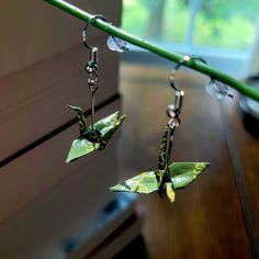 two green origami cranes hanging from hooks on a wooden table next to a window