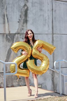 a woman in a green dress is holding gold balloons that spell the number twenty six