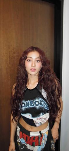 a woman with long red hair standing in front of a wooden door wearing a black shirt