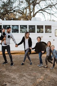 a group of people holding hands and walking in front of a white bus on dirt ground