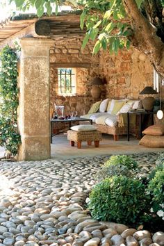 an outdoor living area with stone walls and large tree in the foreground, surrounded by greenery