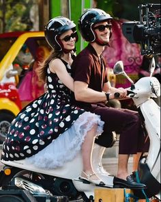 a man and woman riding on the back of a scooter with polka dots