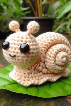 a crocheted snail sitting on top of a green leaf