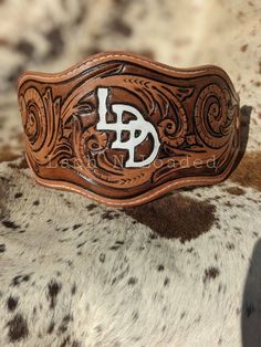 a brown and white cowhide belt with the letter b in it's center