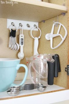 kitchen utensils are hanging on the wall behind a cup and mixer in a cabinet