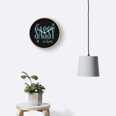 there is a plant on the table next to a lamp and a clock that says sassy be here