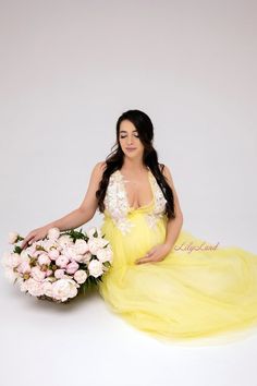 a pregnant woman in a yellow dress holding a bouquet of flowers and posing for the camera