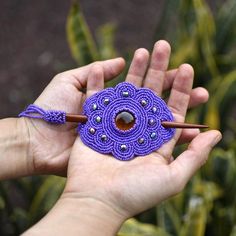 a person holding a purple beaded object in their left hand with a wooden stick sticking out of it